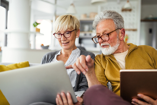 Zwei Personen sitzen auf einem Sofa und benutzen ein Tablet und ein Notizbuch in einem modernen Wohnzimmer.